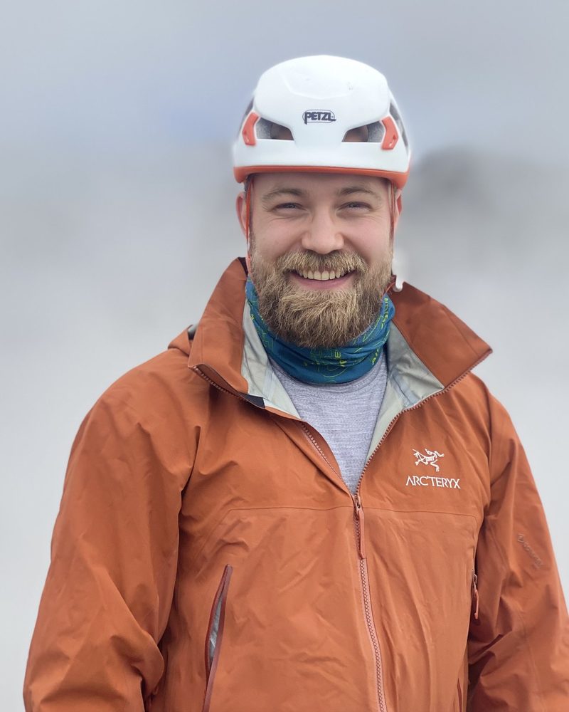 Simeon Schemenauer mit Kletterhelm, lächelnd, im Nebel am Berg